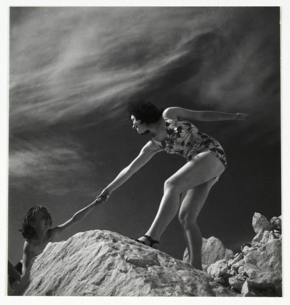 Woman helping child climb onto a rock, about 1935
